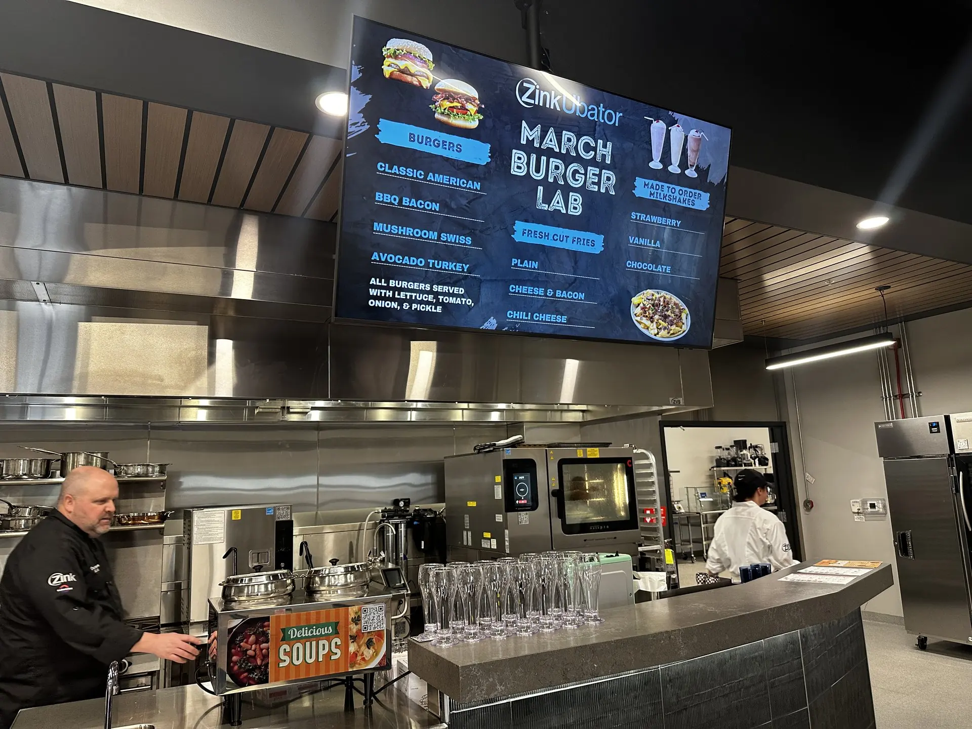 A ZinkUbator burger lab — the menu board over a live station