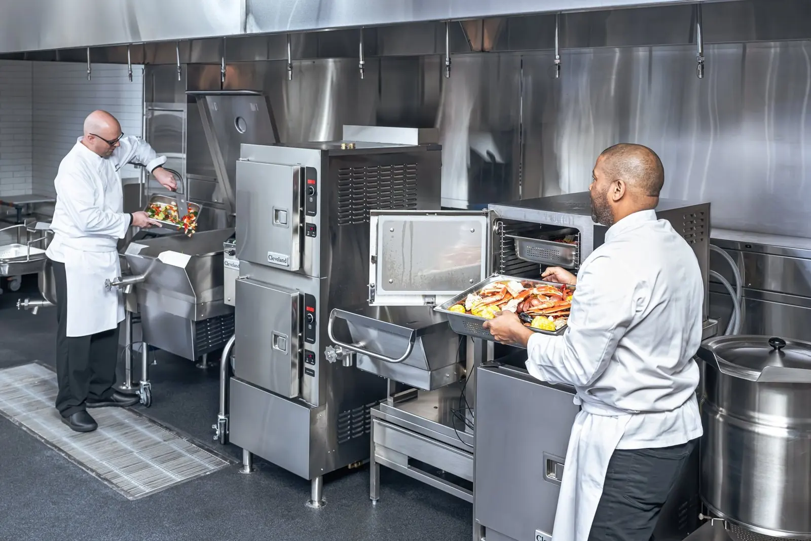 Two chefs working a bank of Cleveland kettles and a tilt skillet
