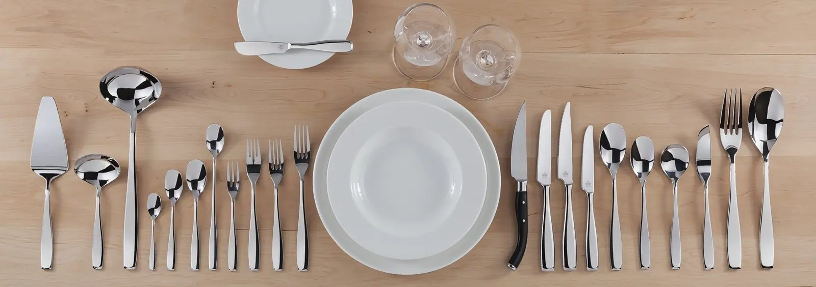 A full banquet place setting of flatware laid out on wood